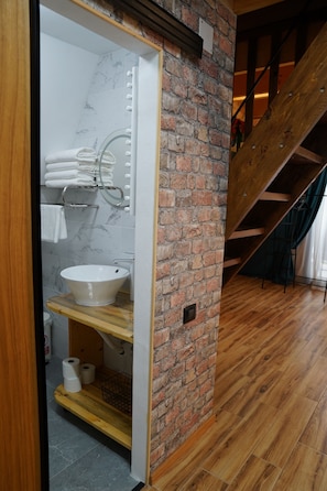 A bathroom with a marble-tiled wall, a white sink, and a wooden vanity.