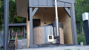A cylindrical structure with a metal exterior, possibly a sauna or water heater, attached to a building with a wooden interior and a metal roof.