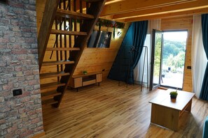 A room with a wooden staircase, a flat-screen TV mounted on a wall, a small table with a plant, and a large window with curtains.