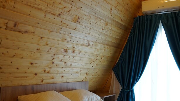 A room with a sloped ceiling, wooden walls, a bed with white bedding, a nightstand, and a window with curtains.
