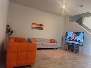 A living room with a sofa, a large flat-screen TV, and a painting on the wall. - Super Spacious 6-bedroom Newly Built Home in Denton (Denton)