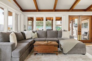 A modern living room with a sectional sofa, a wooden coffee table, and a large window providing natural light.