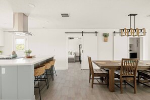 Eine moderne Küche mit einer zentralen Kochinsel, Barhocker und einem Essbereich mit Holztisch und Stühlen.
