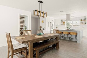 A modern kitchen with white cabinetry, a wooden dining table with benches, and a hanging light fixture.
