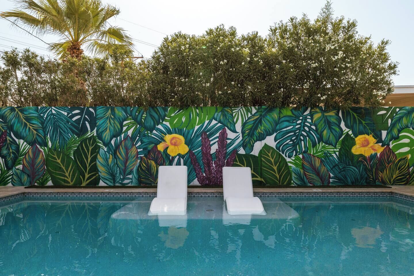 A swimming pool with two white lounge chairs and a mural of tropical foliage and flowers on the wall.