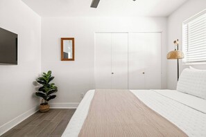 A bedroom with a bed, a wardrobe, a mirror, and a potted plant.