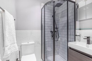 Un baño moderno con ducha de mampara de vidrio, inodoro blanco y lavamanos con espejo.