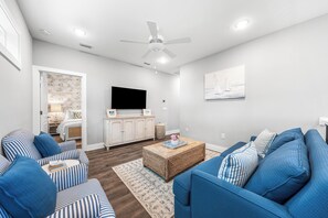 Uma sala de estar moderna com televisão de tela plana, sofás azuis, uma mesa de centro de madeira e um ventilador de teto.