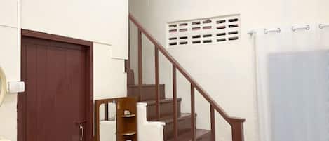 A staircase with wooden steps and a handrail, a brown door, and a white wall with a small window.