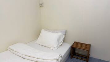 A small, single-bed room with a wooden nightstand and a wall socket.