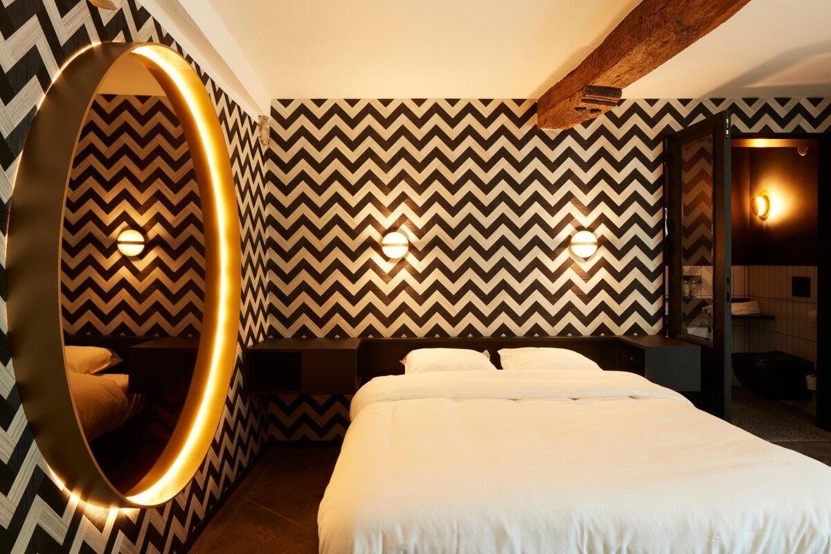 Ein Hotelzimmer mit einem großen Bett, einem runden Spiegel und einer chevron-geahmten Wand.