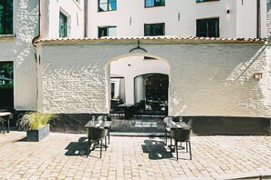 Ein Patio im Freien mit Tischen und Stühlen, einer Steinmauer und einem Durchgang zu einem Innenbereich.