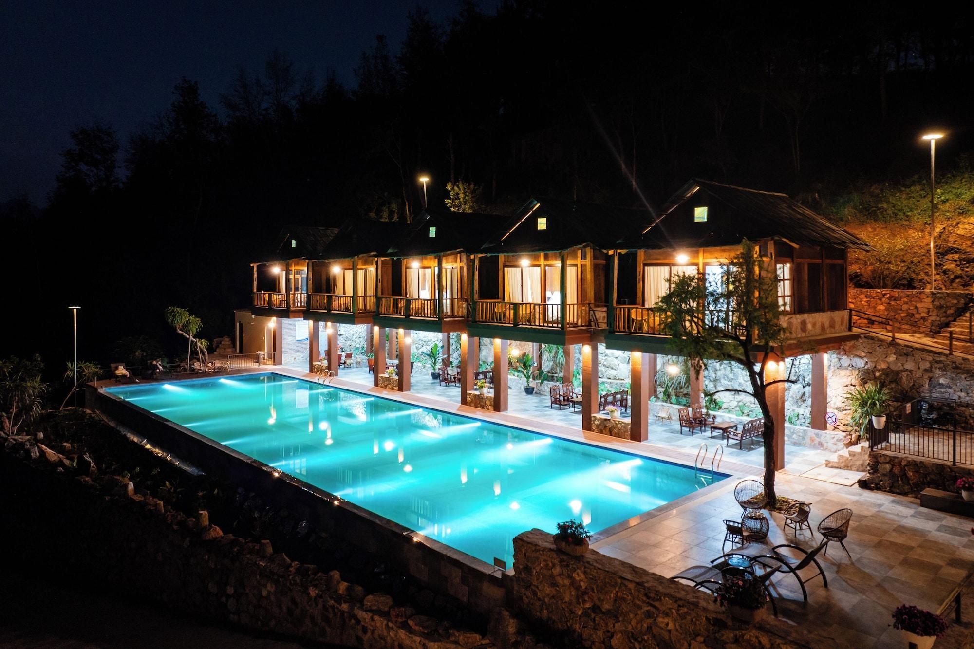 A two-story building with a swimming pool, outdoor seating, and a stone wall.