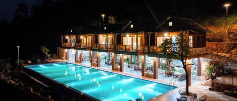 A two-story building with a swimming pool, outdoor seating, and a stone wall.