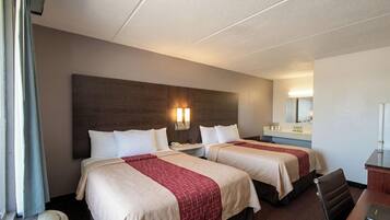 A hotel room with two beds, a desk, a chair, a mirror, and a window with curtains.