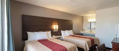 A hotel room with two beds, a desk, a chair, a mirror, and a window with curtains.