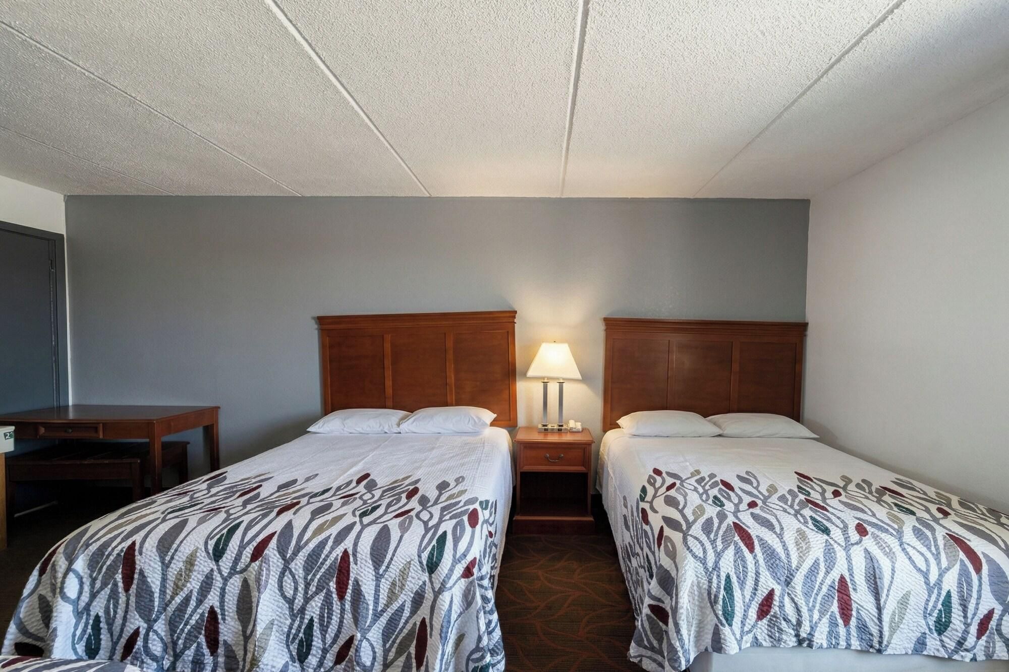 A hotel room with two single beds, a nightstand with a lamp, and a desk.