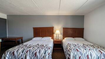 A hotel room with two single beds, a nightstand with a lamp, and a desk.