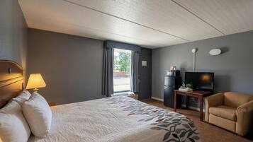 A hotel room with a bed, a desk, a television, a chair, and a window with curtains.