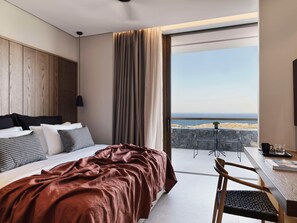 A modern hotel room with a large bed, a desk with a chair, and a balcony with a view of the sea. - Magma Resort Santorini in of the Unbound Collection by Hyatt (Santorini)