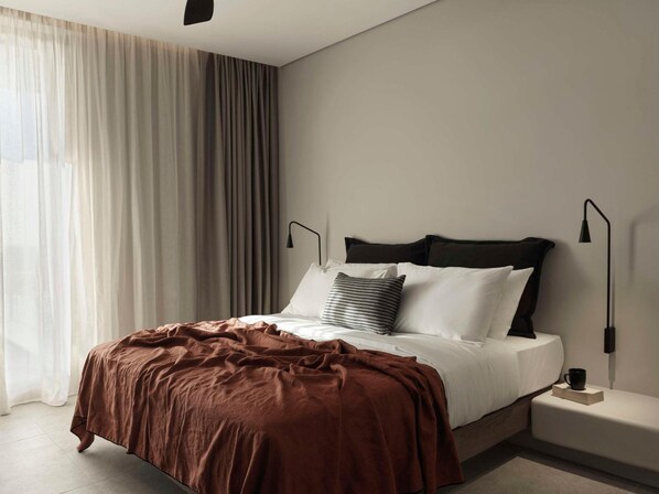 Une chambre moderne avec un grand lit, une table de chevet, une lampe et une fenêtre avec des rideaux.