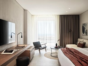 Habitación de hotel moderna con una cama grande, un escritorio con televisor de pantalla plana, una silla, una pequeña mesa redonda y vistas al exterior.