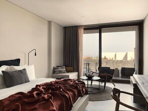 A modern hotel room with a large bed, a sofa, a dining area, and a balcony with a city view. - Magma Resort Santorini in of the Unbound Collection by Hyatt (Santorini)