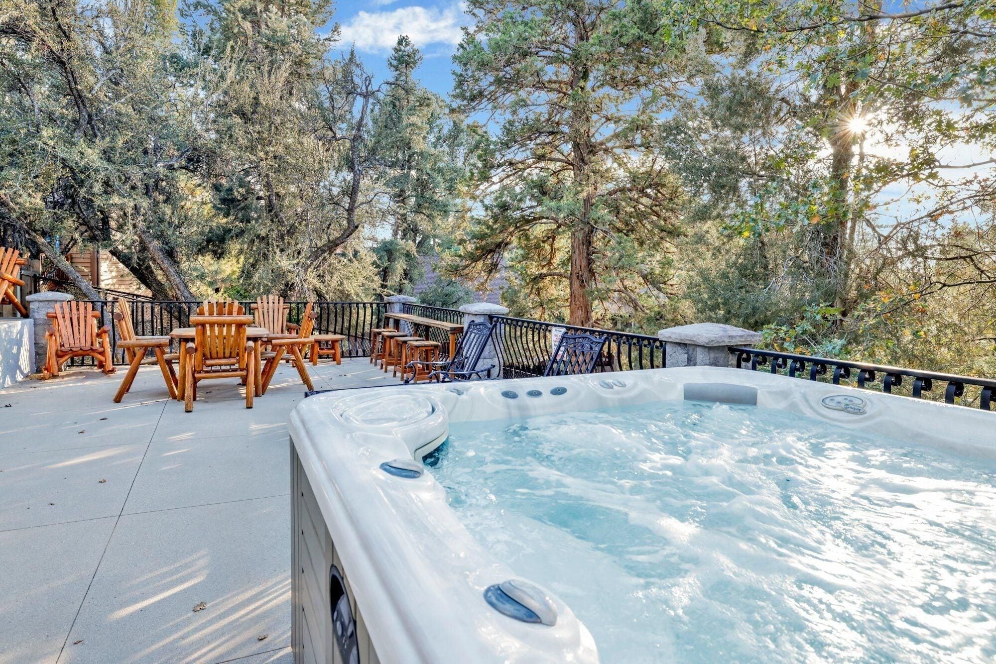 Een hottub op een terras, met stoelen en een leuning, omgeven door bomen.