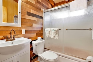Un baño con panel de pared de madera, un lavamanos blanco, un inodoro y un box de ducha de vidrio.