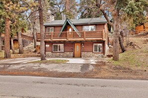 A two-story log cabin with a balcony, stone foundation, and a clear driveway. - Bear Tracks #2020 (Big Bear Lake)