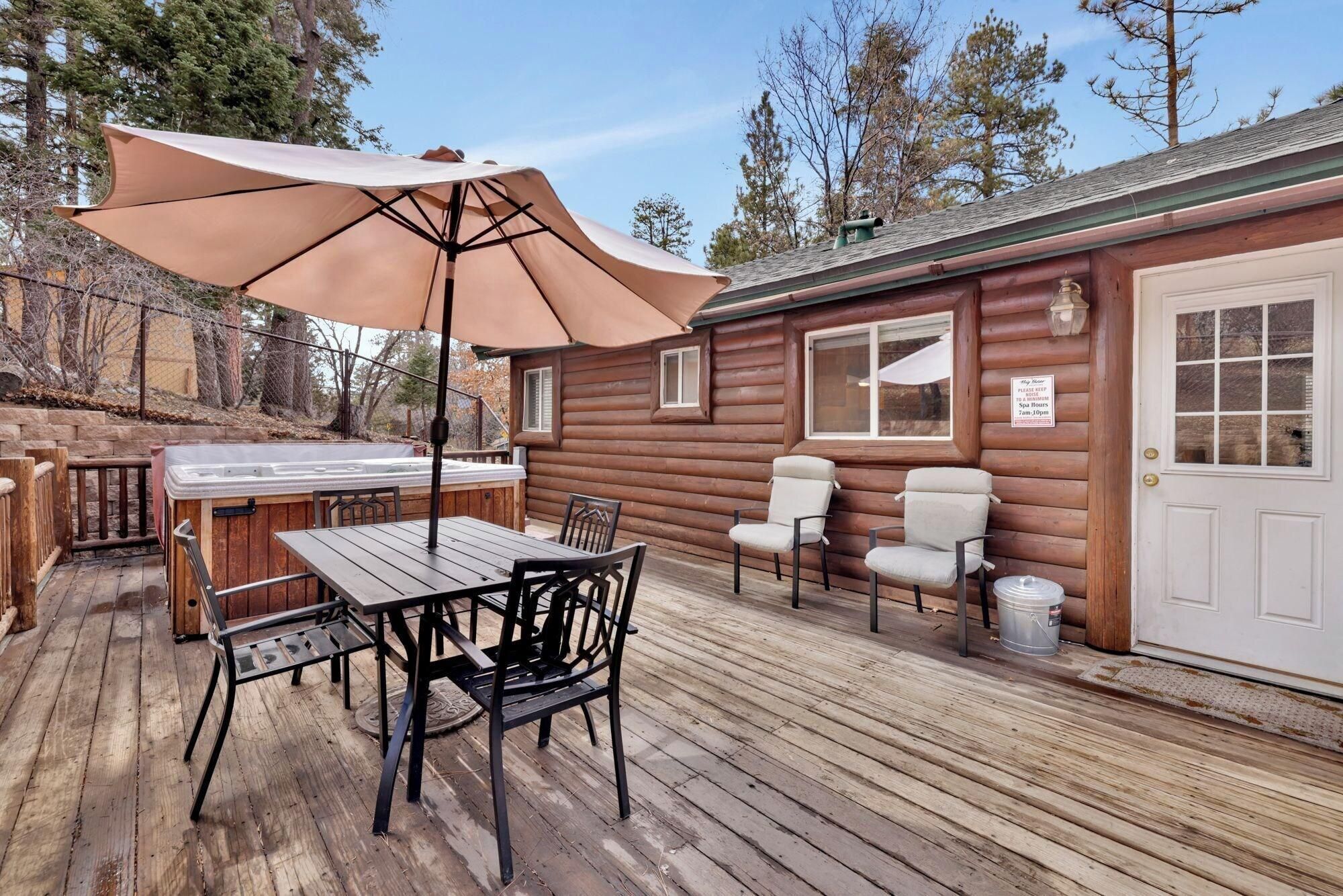A wooden deck with a table and chairs, a hot tub, and a covered area with an umbrella.