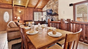 Un comedor de madera con una mesa dispuesta para dos, una pared de piedra y una televisión sobre la chimenea.