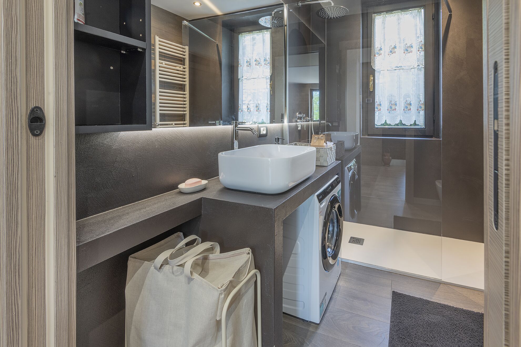 A modern bathroom with a large mirror, a white sink, a towel rack, and a washing machine.