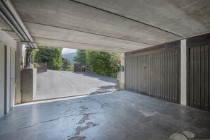 A covered parking area with a concrete floor, a gated entrance, and a view of a mountainous landscape. - AffittiPontediLegno - Fumeclo (Temù)