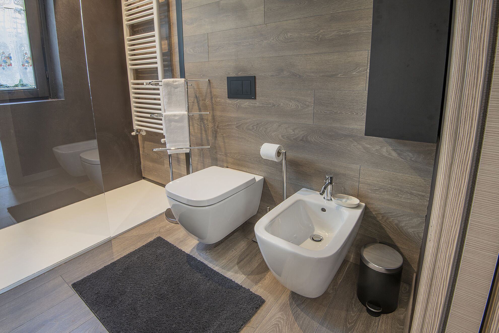 A modern bathroom with a toilet, bidet, and a glass shower enclosure.