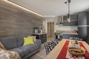 A modern kitchen with dark cabinets, a wooden countertop, and a dining area with a red runner. - AffittiPontediLegno - Fumeclo (Temù)