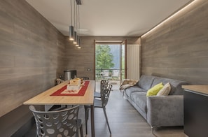 A modern interior with a dining area, a sofa, and a view through a glass door. - AffittiPontediLegno - Fumeclo (Temù)
