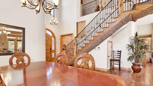 Un comedor amplio con una gran mesa de madera y sillas, una escalera con barandilla de madera, y un candelabro.