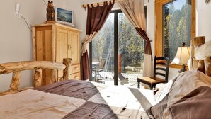 Un dormitorio con estructura de cama de madera, un televisor sobre un mueble de madera, una ventana con cortinas y vistas al exterior.