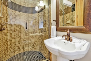 Une salle de bain avec une douche à parois de verre, un lavabo blanc et un miroir avec un cadre en bois.