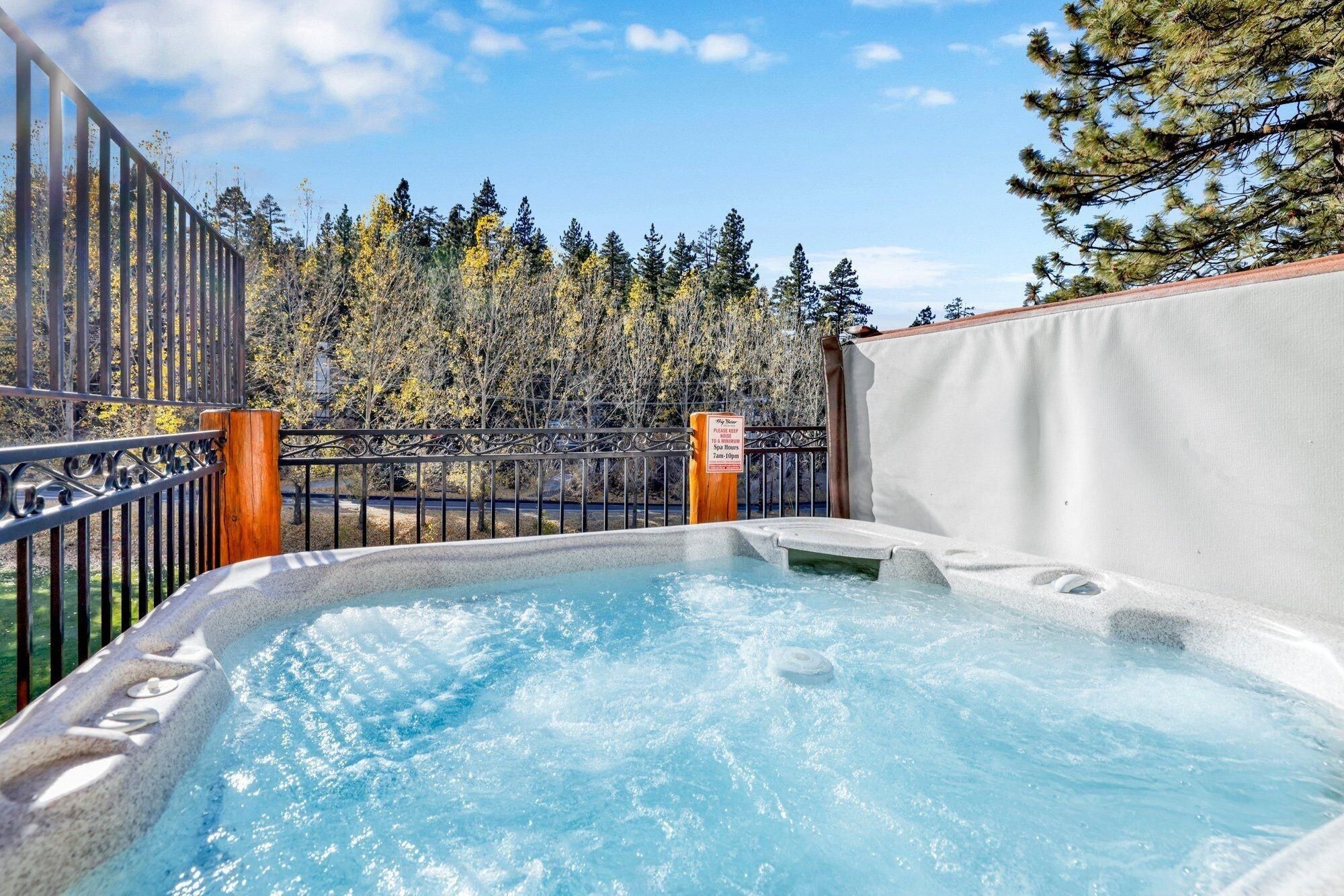 Un bain à remous avec vue sur une forêt et une clôture en métal.