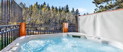 A hot tub with a view of a forest and a metal fence.