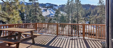 A wooden deck with a picnic table and a railing overlooking a snowy mountain landscape.