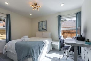 A bedroom with a bed, a desk, a chair, a desk lamp, and a window with curtains. - Marbella Lane Convenient Home In Sunnyvale (Sunnyvale)