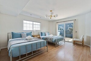 Un dormitorio con dos camas, una ventana, una lámpara en el techo y una puerta corrediza de vidrio que da a un área exterior.