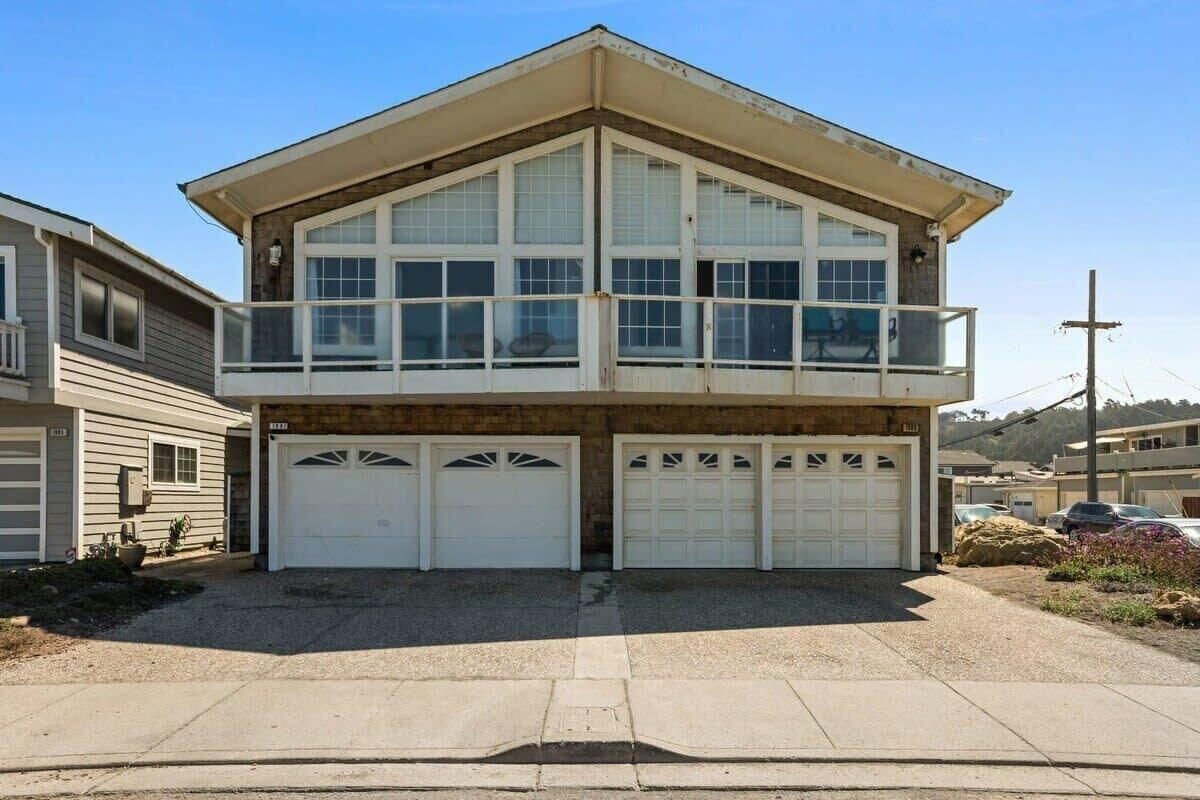A two-story residential building with a balcony, three garage doors, and a driveway.