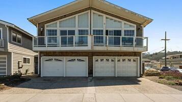 A two-story residential building with a balcony, three garage doors, and a driveway.