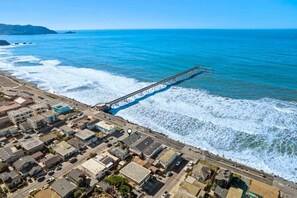 Uma cidade costeira com um cais que se estende para o mar, rodeada por edifícios residenciais e um céu limpo.