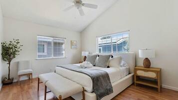 A bedroom with a bed, bedside tables, a bench, a ceiling fan, and windows.