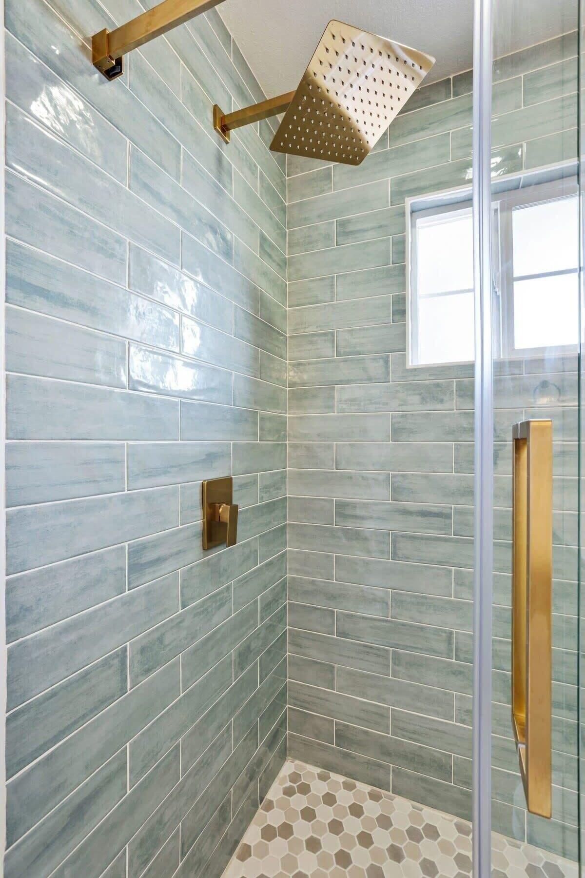 A shower with a glass door, a gold showerhead, and a tiled wall.